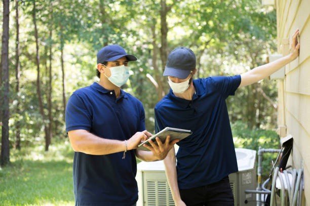 Two pest control technicians wearing face masks and navy blue shirts conducting a free pest control inspection using a tablet outside a residential home in Kearney, Nebraska.