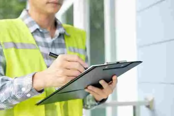 A professional provider of residential pest services filling out a structural inspection checklist on a clipboard outside a home.